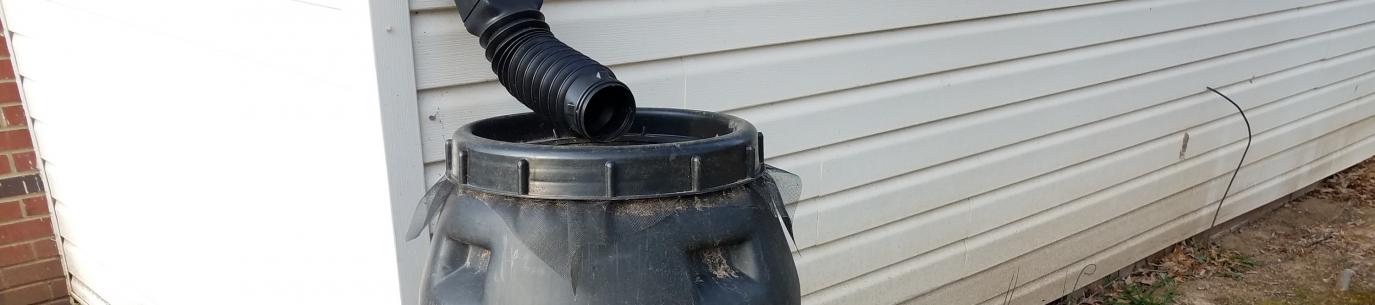 black rain barrel next to white house, build your own rain barrel for your climate victory garden